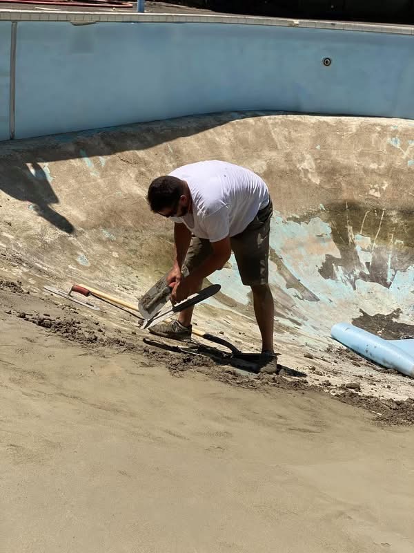 Crew member hand-troweling the floor of a pool under renovation